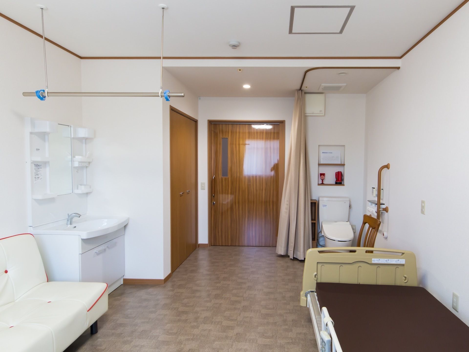 居室の入口近くに、カーテンの仕切りがついたトイレが設置されている。洗面台の近くに、物干し棒が吊り下げられている。