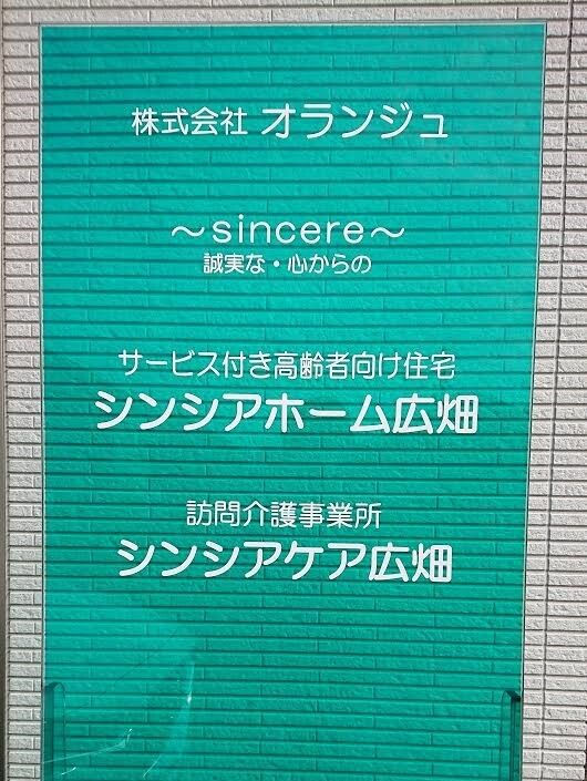 掃き出し窓の近くにガラス板の看板が設置されている。施設名称の上に、名称にちなんだ花の絵が赤い線で描かれている。