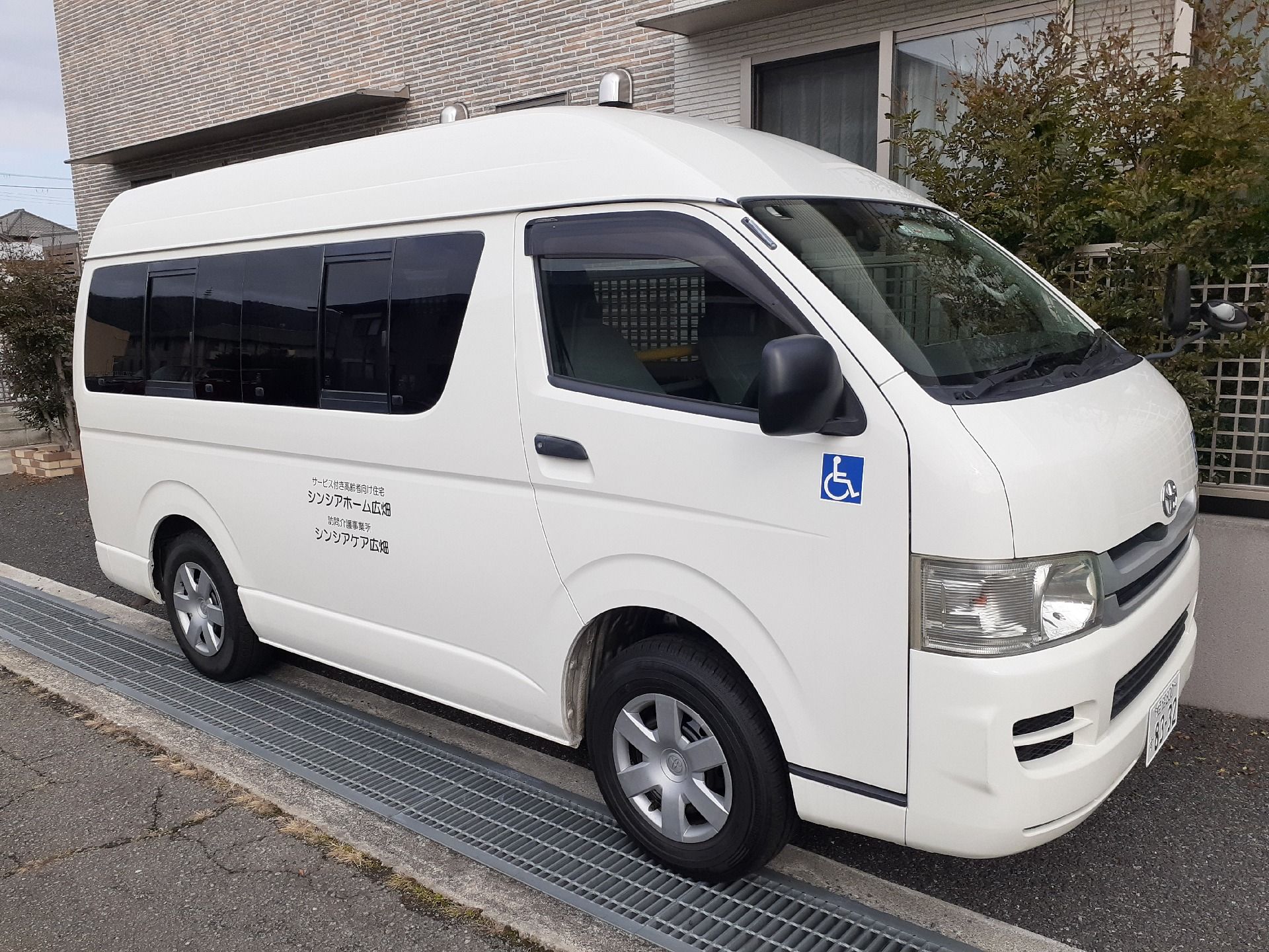 建物の横に駐車している、施設名が書かれた白いワゴン車
