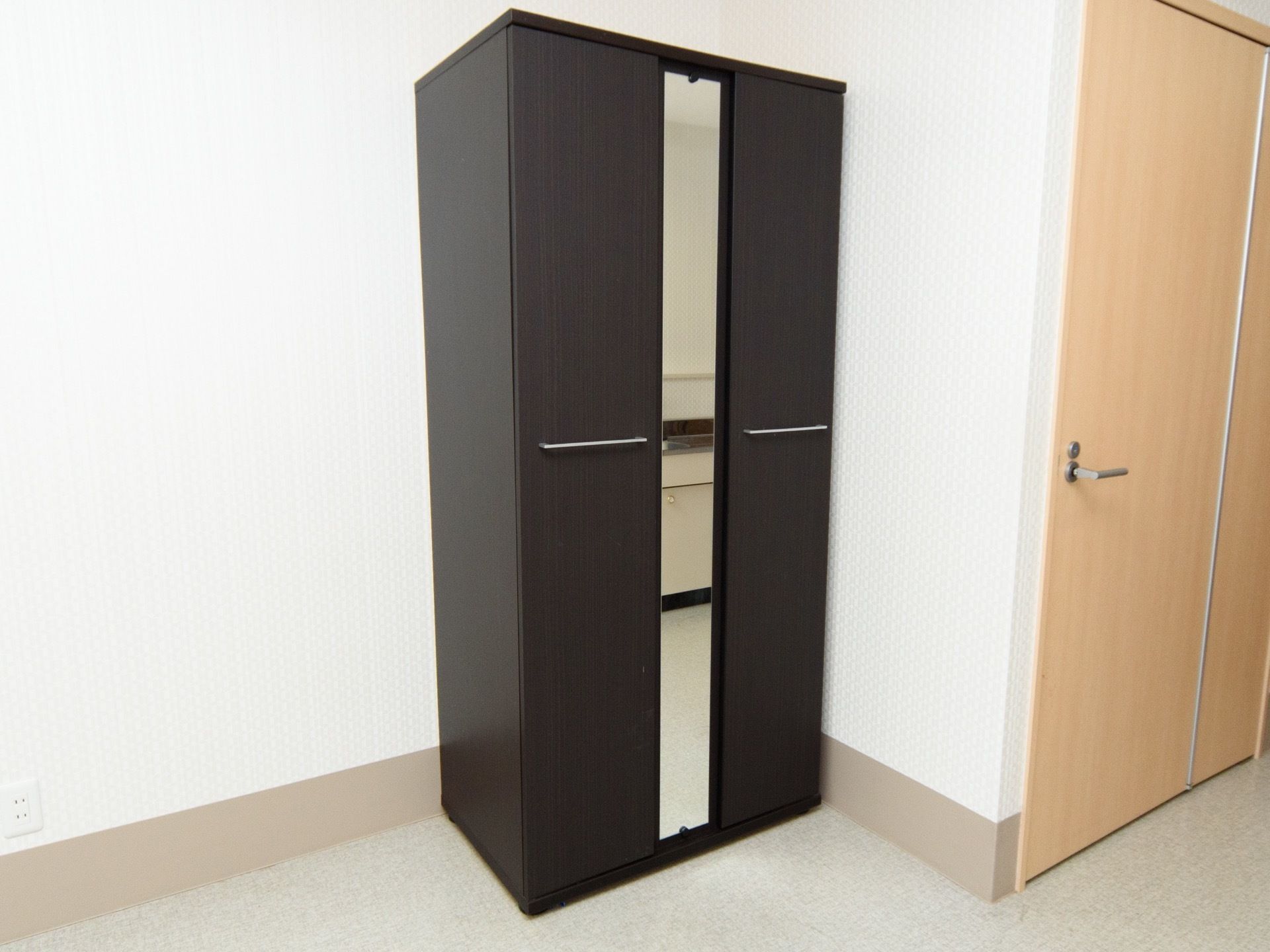 白い壁の個室タイプの居室で、部屋のコーナーに黒いクローゼットが置かれている。左右の扉の間に縦長の鏡が取り付けられている。