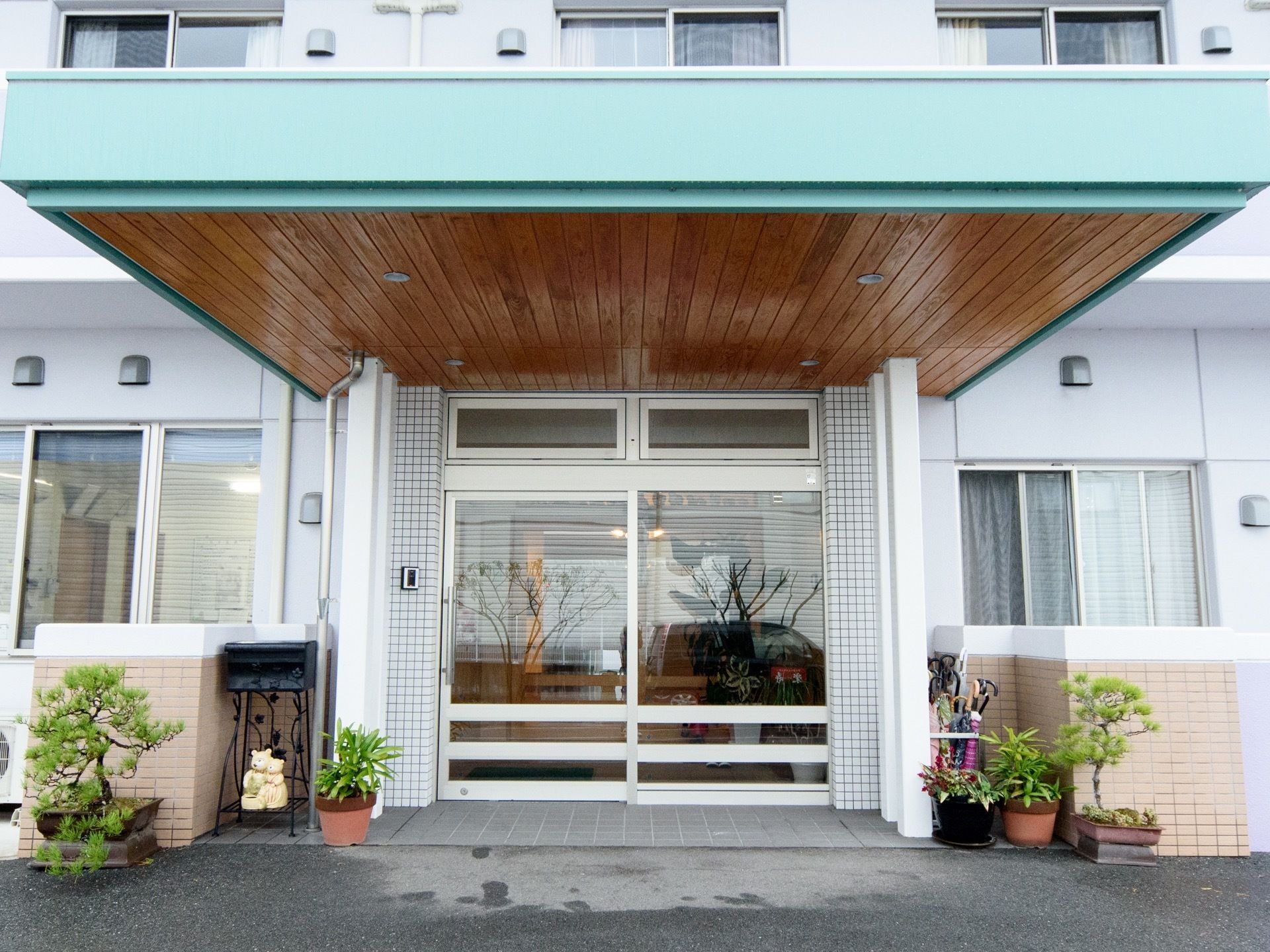 玄関には大きなひさしが設けられていて、埋め込み式の小さなライトが４つ設置されている。玄関ドアの両脇に植物が置かれている。