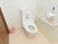 トイレの壁は、淡い色調の草花柄の壁紙が使用され、ペーパーホルダーと手すりが取り付けてある。洋式便座の左側に小さな籠が置かれている。