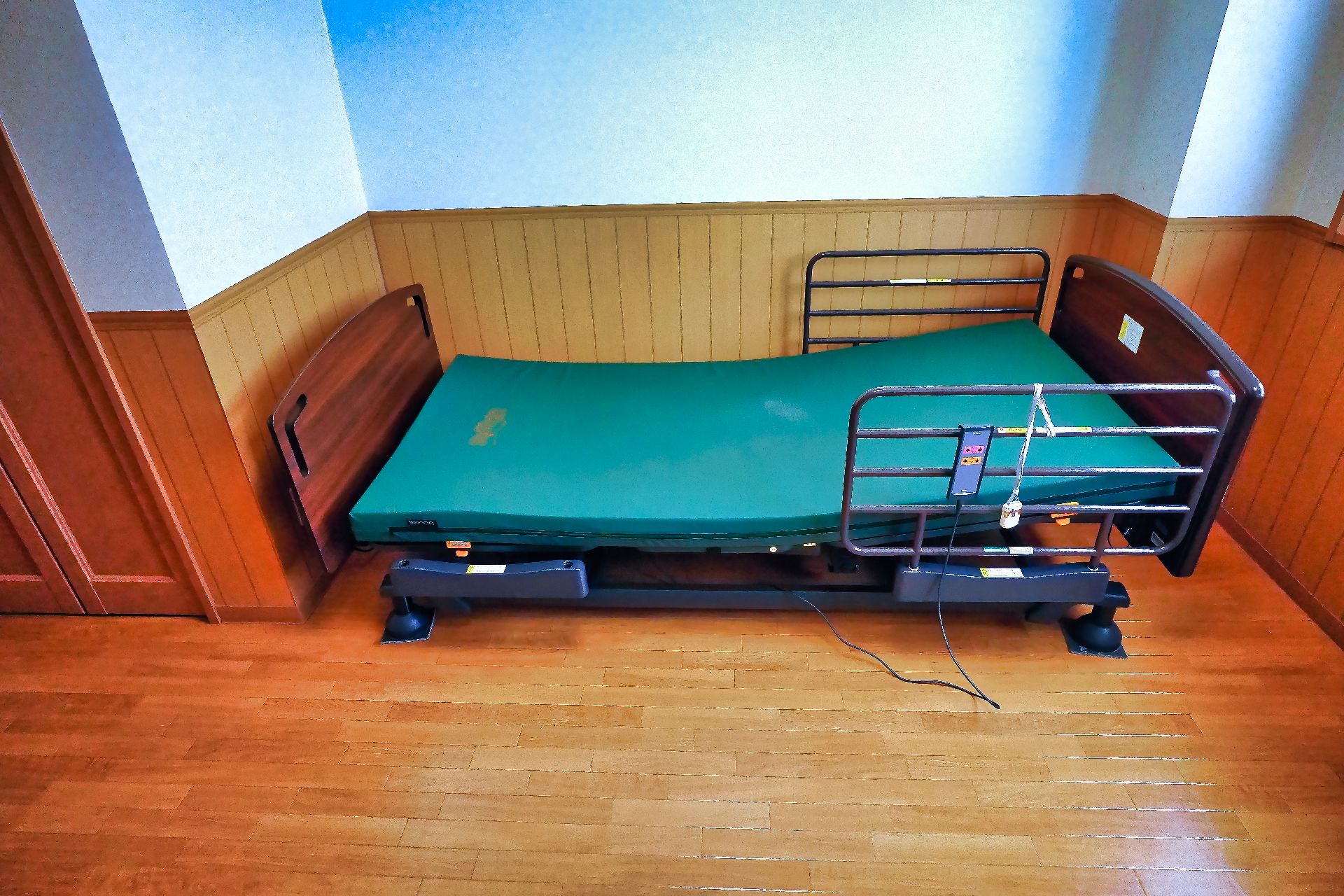 白い壁沿いに置かれた緑のマットレスが敷かれた柵のあるベッド