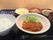 玉ねぎソースがかかったメインの料理にはサラダが添えられ、周りには果物や漬物、野菜の和え物、白いご飯、汁物などが並んでいる。