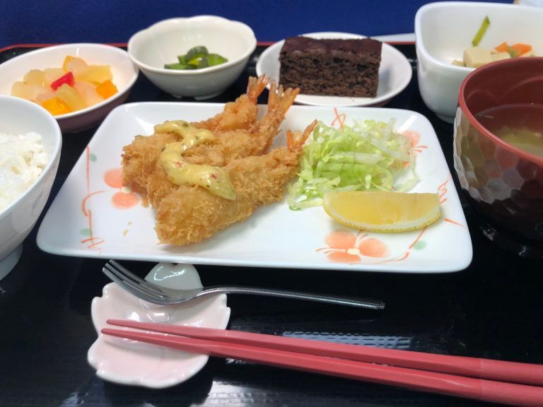 レモンを添えた海老フライとご飯と味噌汁とフルーツのデザート