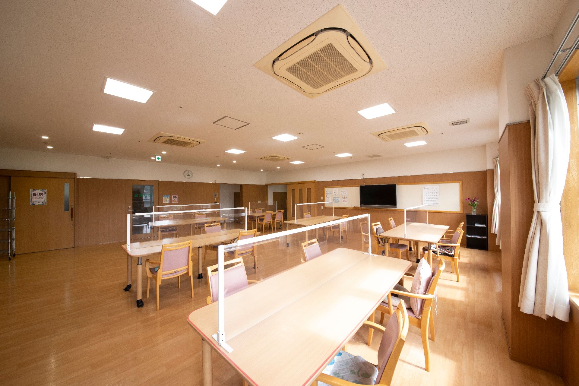 屋外で笑顔で過ごしている車いすの高齢女性と付き添いの若い女性スタッフ。日当たりのいい場所。