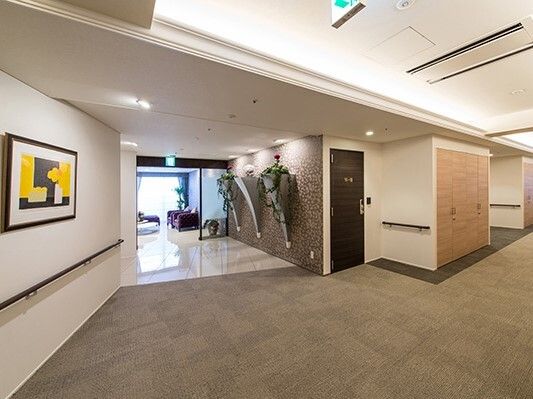 黒と黄色の絵画が飾られた白い壁にはダークブラウンの手すりが付き、奥には日当たりのいい談話室があり、紫のソファの応接セットが置かれている。