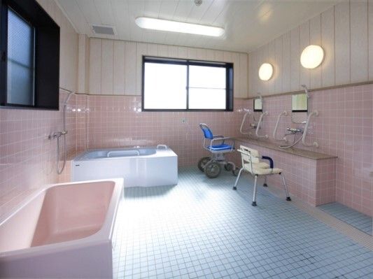 清潔に整えられている施設内の浴室。奥の方に２つの浴槽、右側にシャワーチェアがある様子