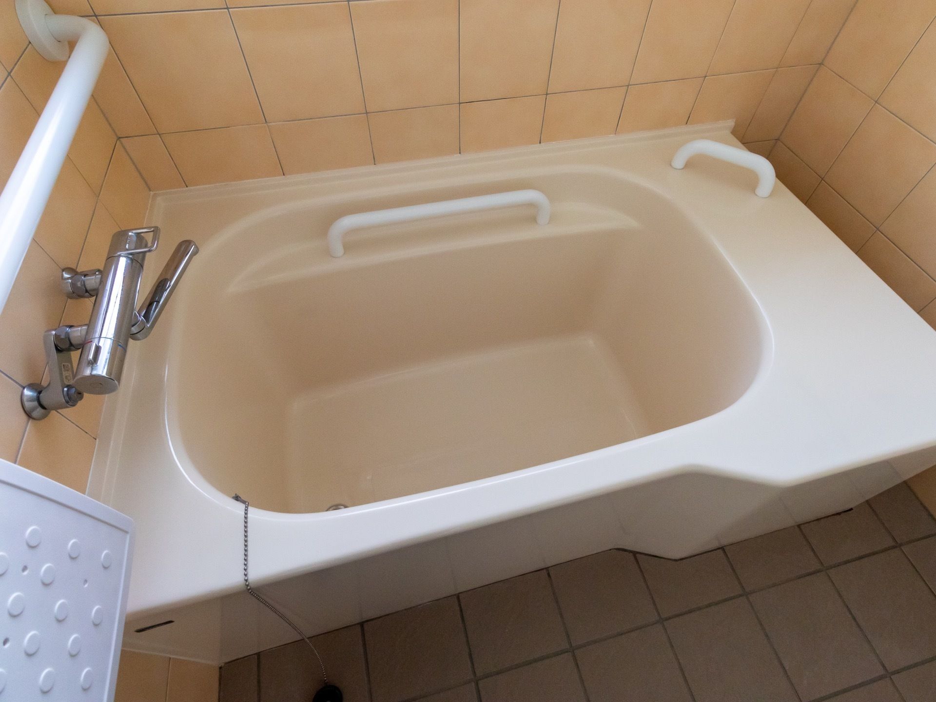 壁と床がタイル張りの浴室に浴槽が設置されている。手すりが複数あり、立ち上がる際につかまることができる。