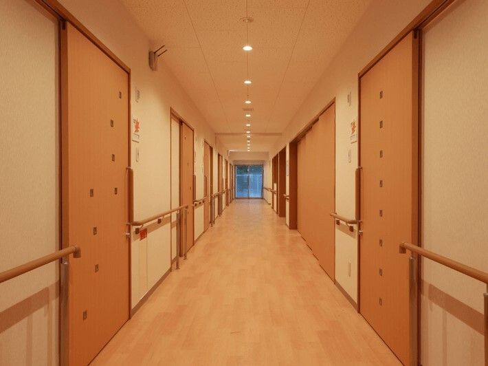 両サイドに手すりと居室のドアが設置されたまっすぐな廊下。居室のドアには小さな明かり窓が付いていて、居室により窓の配列が異なる。