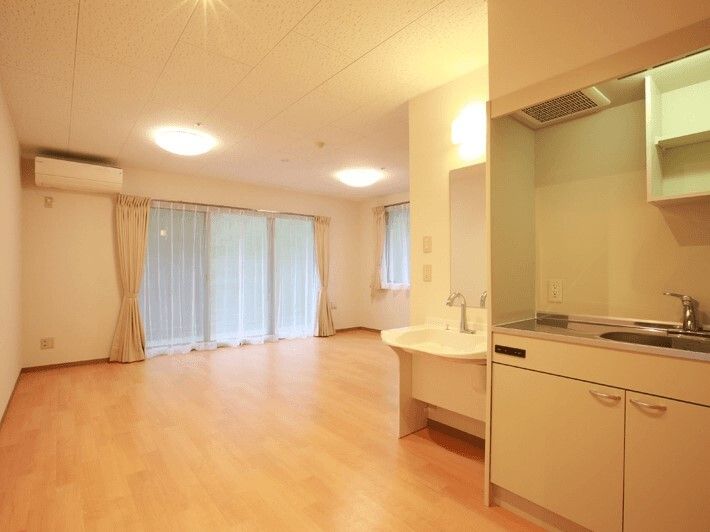 大きな窓が二つ付いたフローリングの部屋にはエアコンやキッチンが付き、窓にはレースカーテンとカーテンが付いていて明るい雰囲気。