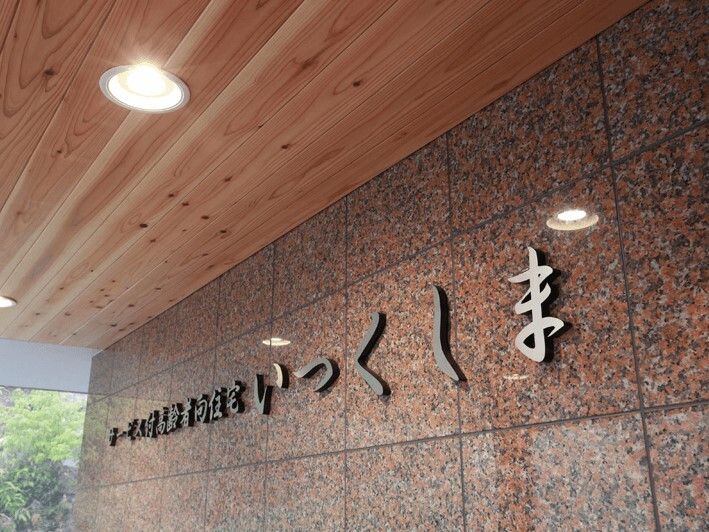 住宅名がシルバーの立体的な文字で書かれていて、大理石のようなブラウンの外壁。木製の天井には照明が付いていて明るい。