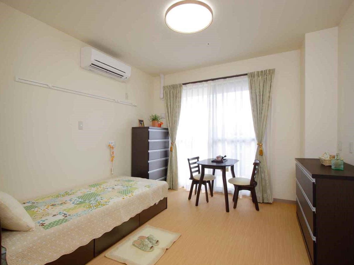 ベッドやタンス、いすなどが置いてある部屋の様子。窓がある明るい部屋の写真