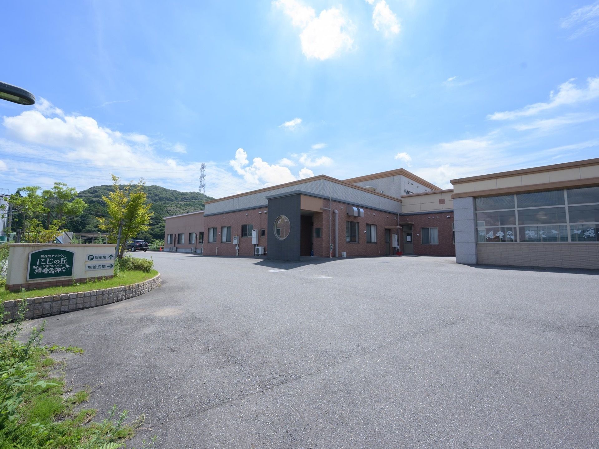舗装された敷地に、一部2階のある平屋建て住宅が建っている。奥の方には駐車スペースがある。