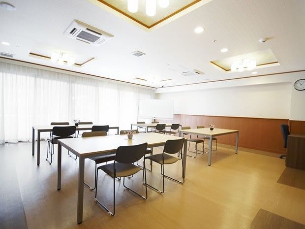 フローリングの床に茶色と白の壁、大きな窓があり明るい雰囲気。テーブルが4つ並べられている。