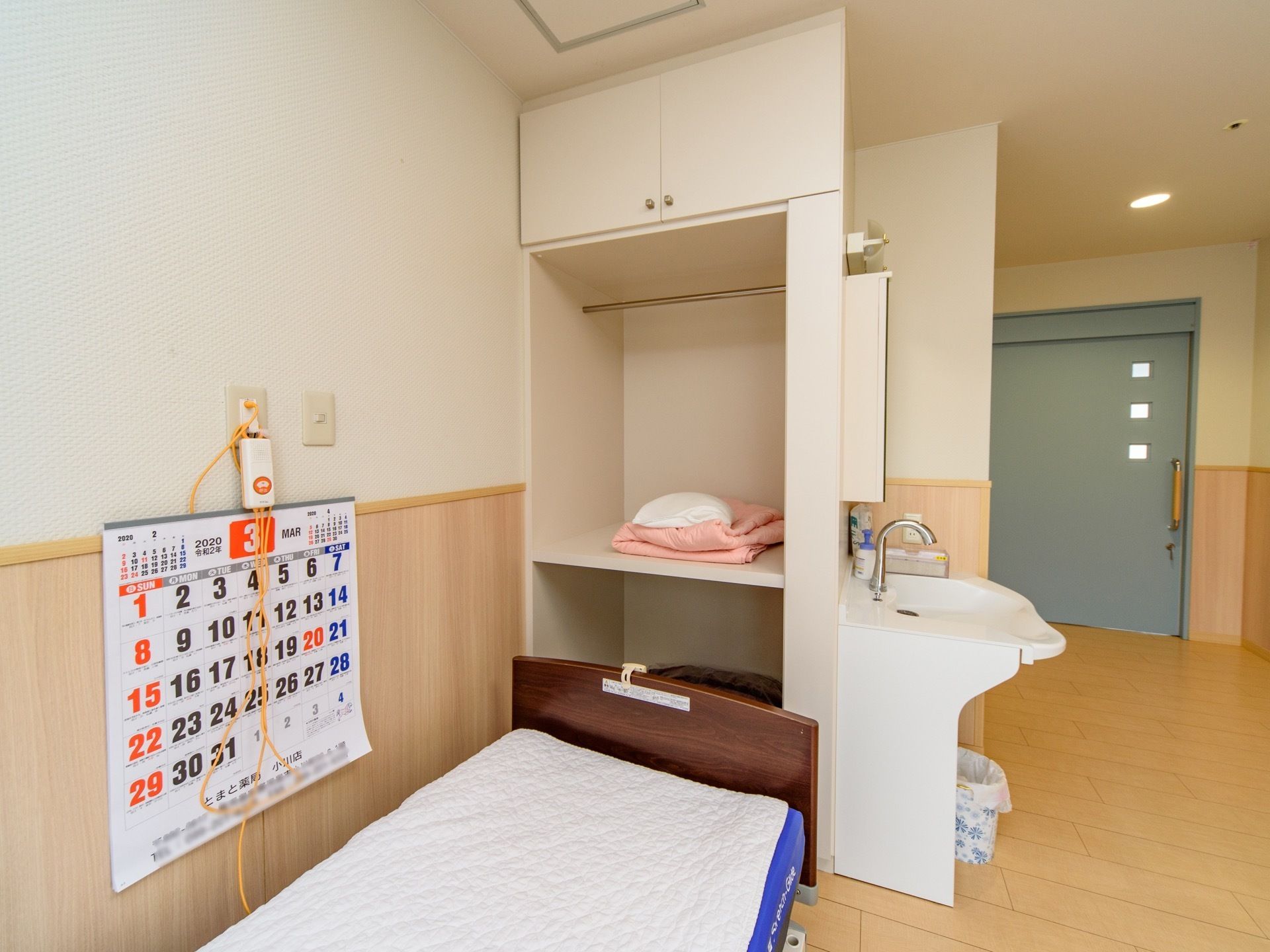 ベッドの側には、大きな棚がありピンク色の毛布と白い枕が置いてある。棚の中には、銀色の突っ張り棒が取り付けている。