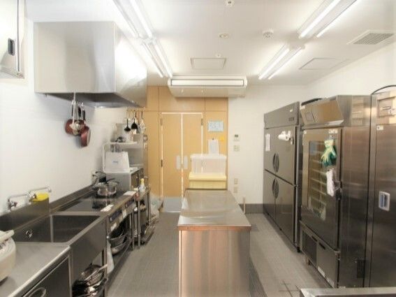 中央に作業台があり、何も置かれていない。左側には業務用の調理器具が並んでいて、左側には流しやコンロがあり、掃除が行き届いている。