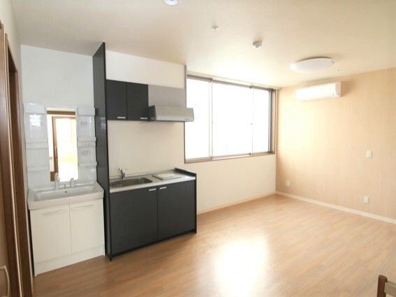 家具や家電はまだ持ち込まれていないフローリングの部屋。エアコンが付き、大きな窓にはカーテンはなく、キッチンと洗面所が並んで設置されている。