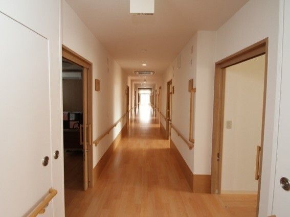 まっすぐな廊下には手すりが付き、居室のドアも両サイドにあり、大きなスライド式のドアが付いている。突き当りには大きなドアがある。