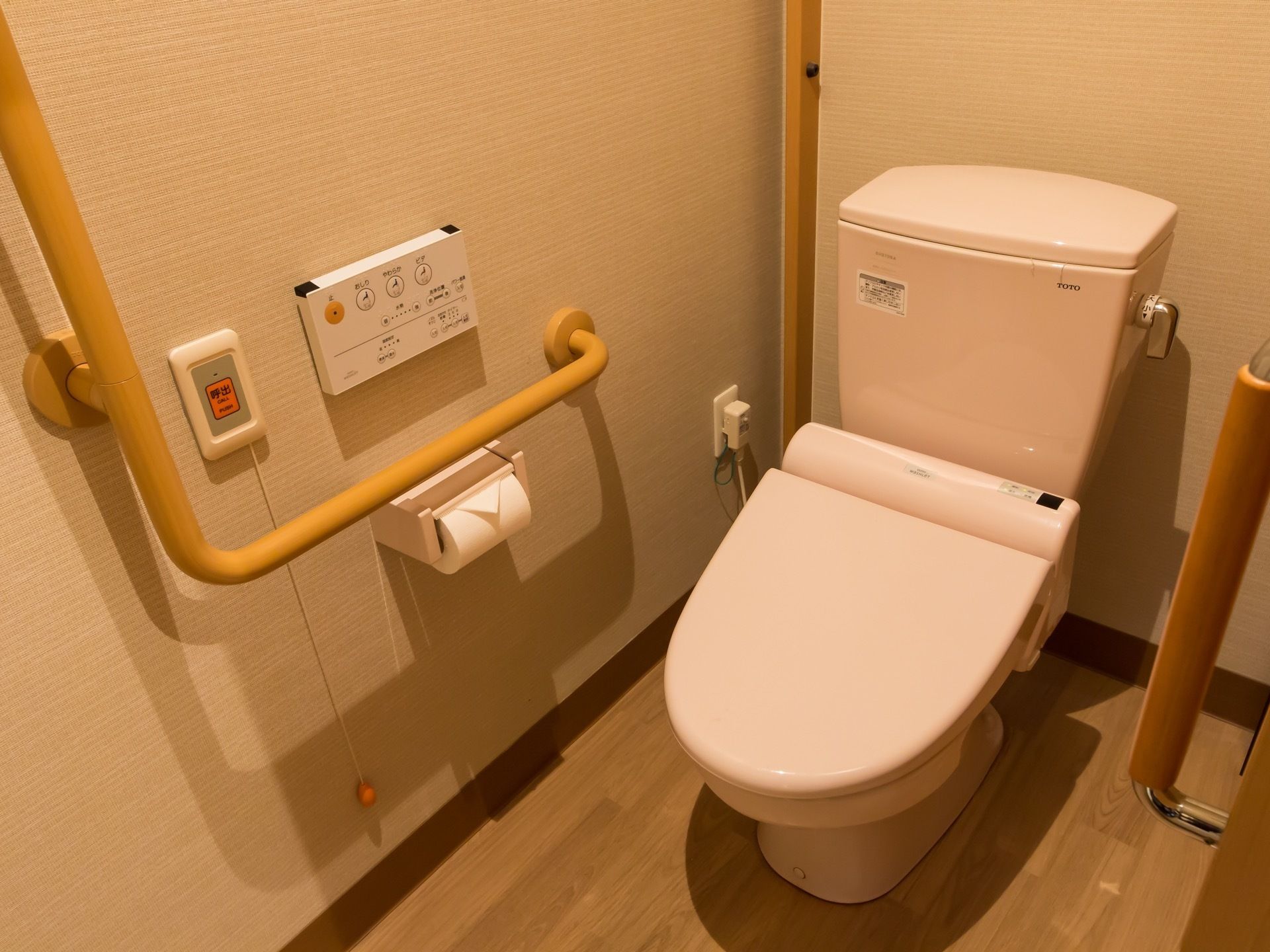 大きな取っ手がついた引き戸を開けるとトイレがある。便座の操作パネルの左側に、ひもがぶら下がった呼び出しボタンがある。