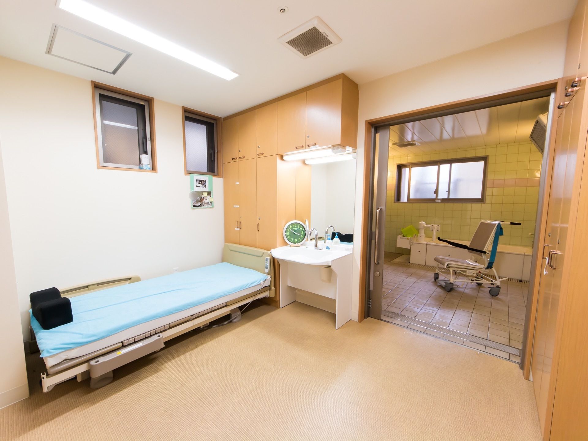 介護浴室は幅の広い入口になっている。脱衣所にはベッドが設置されている。洗面台の脇に時計が置かれている。