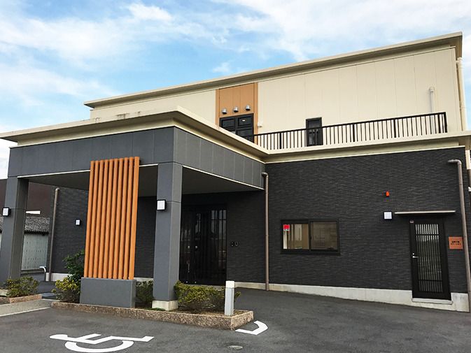 車寄せが付いた2階建ての建物。広い駐車場が付き、2階の部分にはベランダもある。
