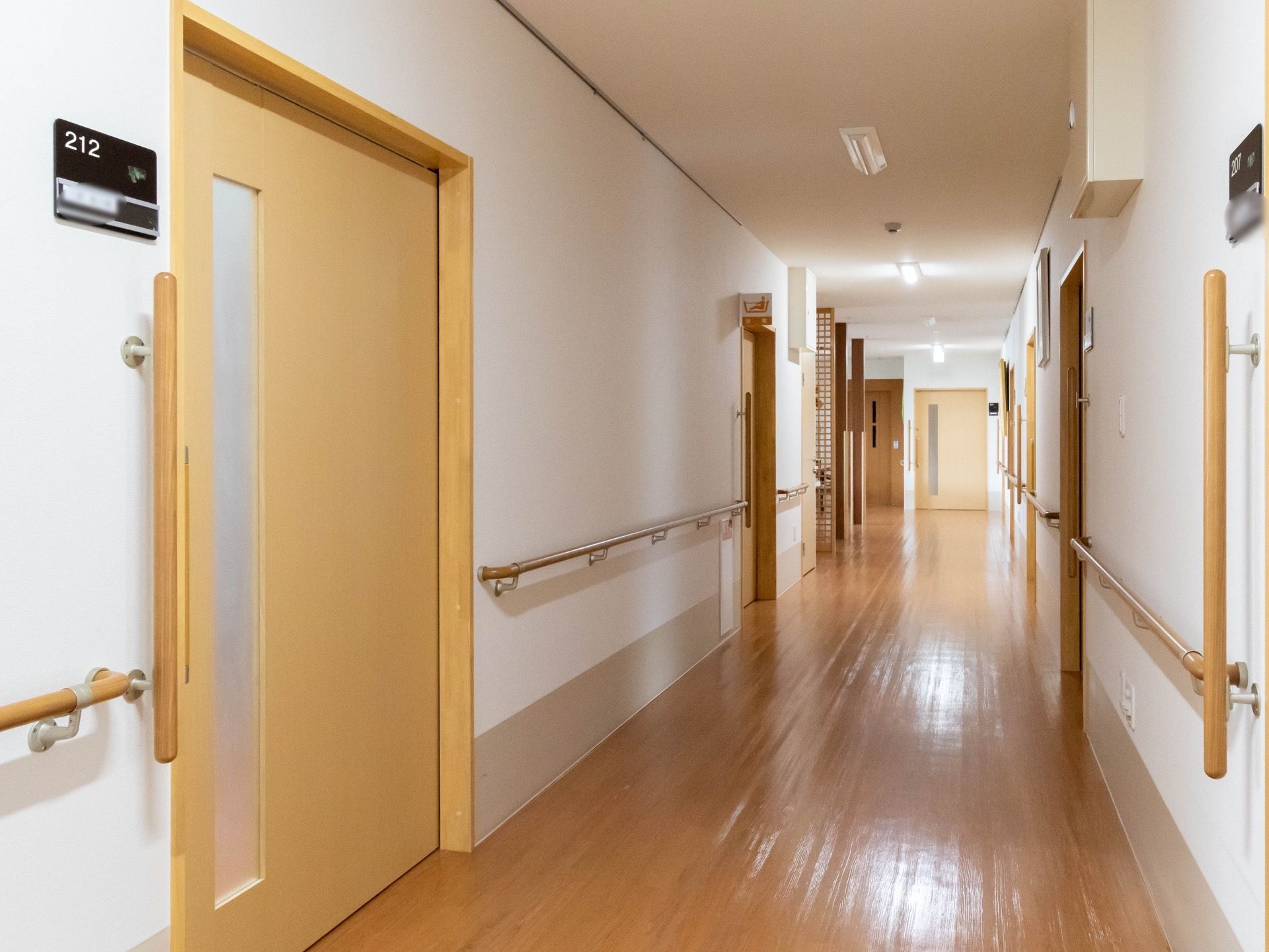 バリアフリーの広々とした廊下である。両サイドに居室が設けられており、壁に沿って手すりがある。
