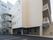 ベージュの建物の側面には屋外階段が設置され、各フロアにベランダも付いている。窓もたくさんある。