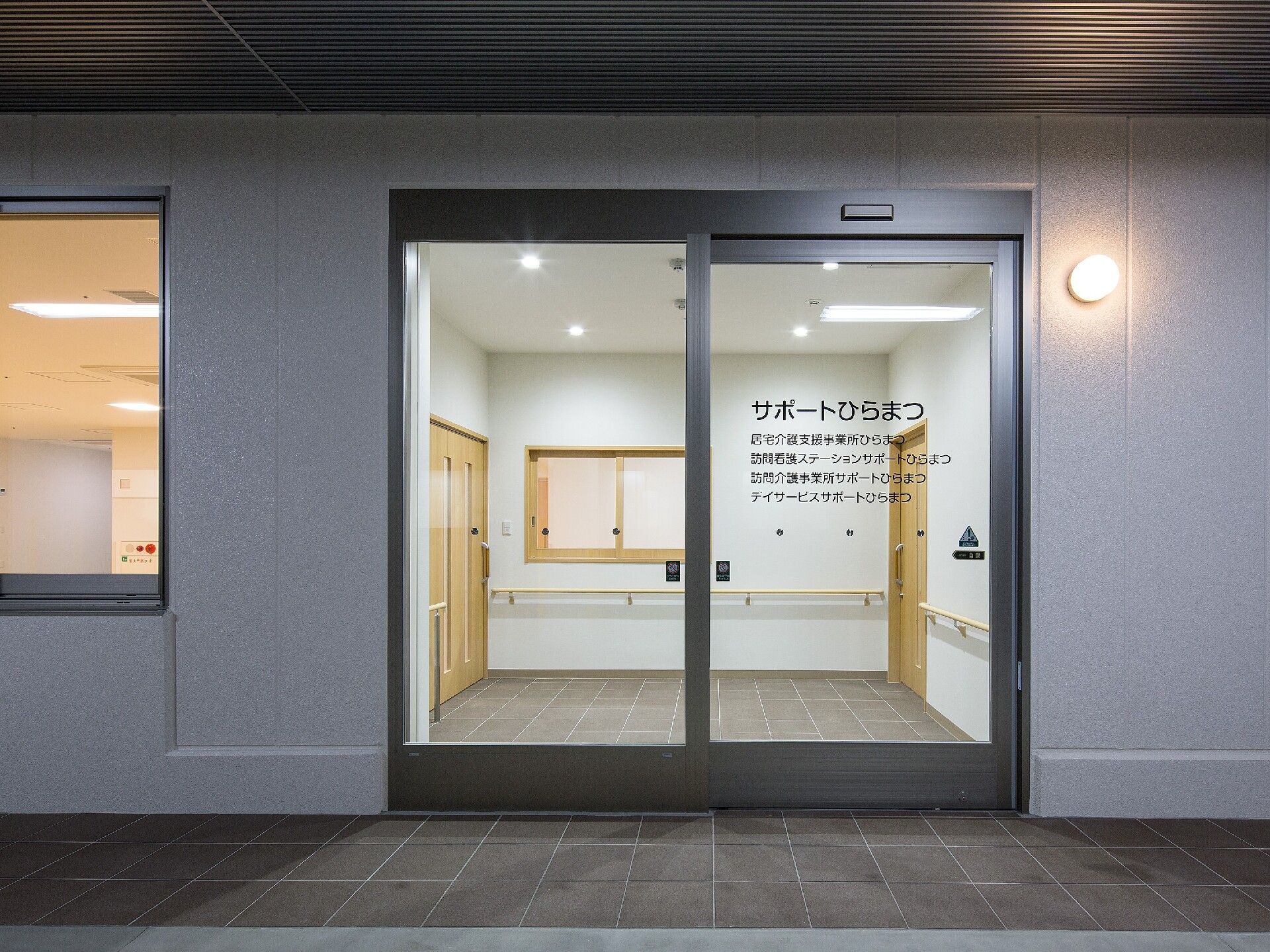 住宅名が書かれた自動ドアが設置された建物の玄関。室内の壁には手すりが付いている。