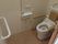 両サイドに手すりと背もたれが付いた便座。壁にはトイレットペーパーホルダーと呼び出しボタンがある。