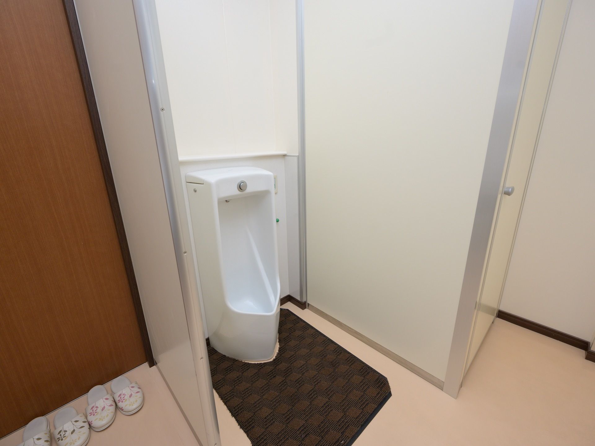 トイレには、スペースが確保されて男性用の小便器がある。足元には、ブラウン系の床汚れ防止マットがある。