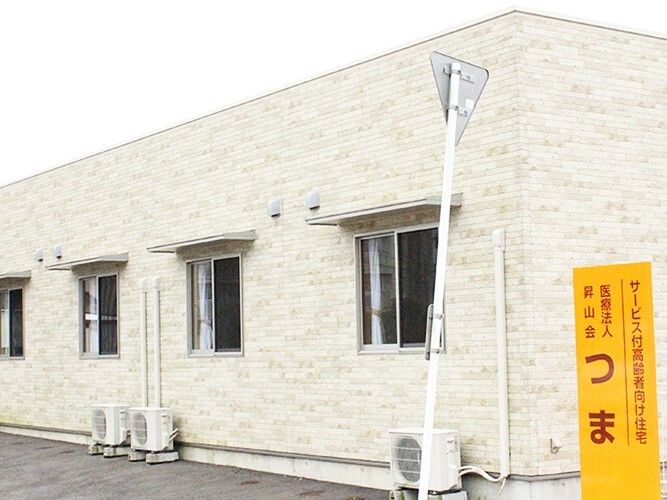 平屋建ての建物は横に長く、アイボリー色のレンガ調の外壁。オレンジの館銘板が建っている。