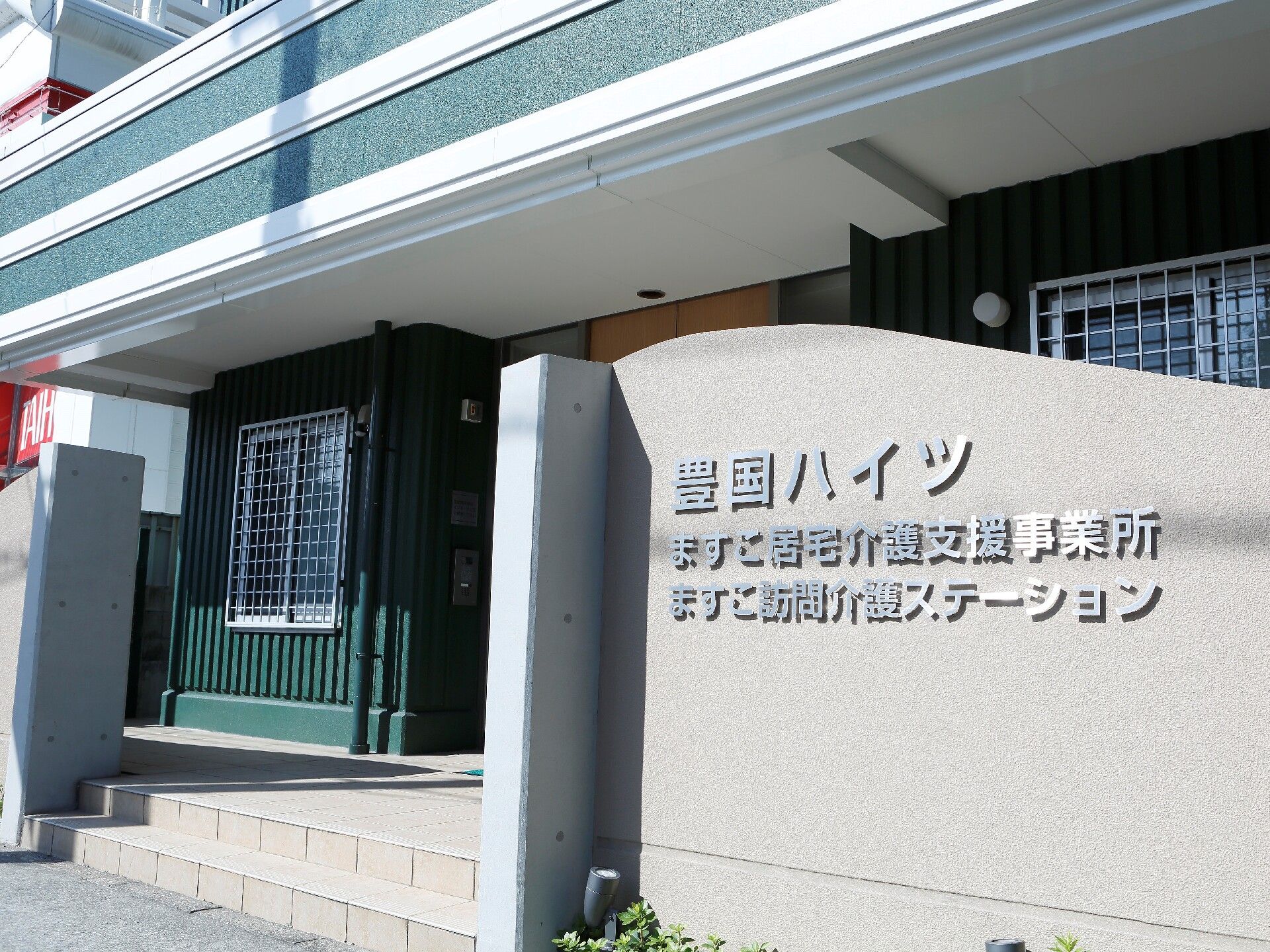 グレーの外壁に併設の訪問介護ステーションと居宅介護支援事業所の名前が書かれている。