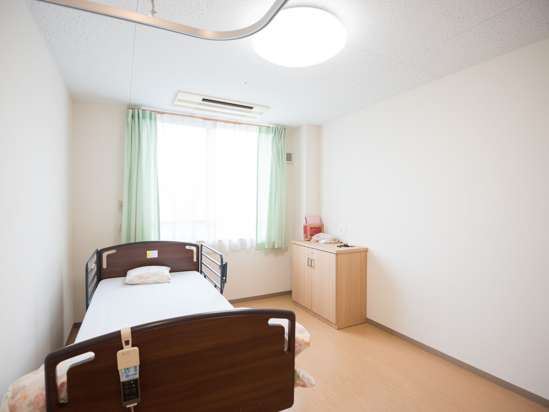 居室には介護ベッドと収納棚が置かれている。大きな窓からは日がたっぷり差し込む。エアコンが完備されている。