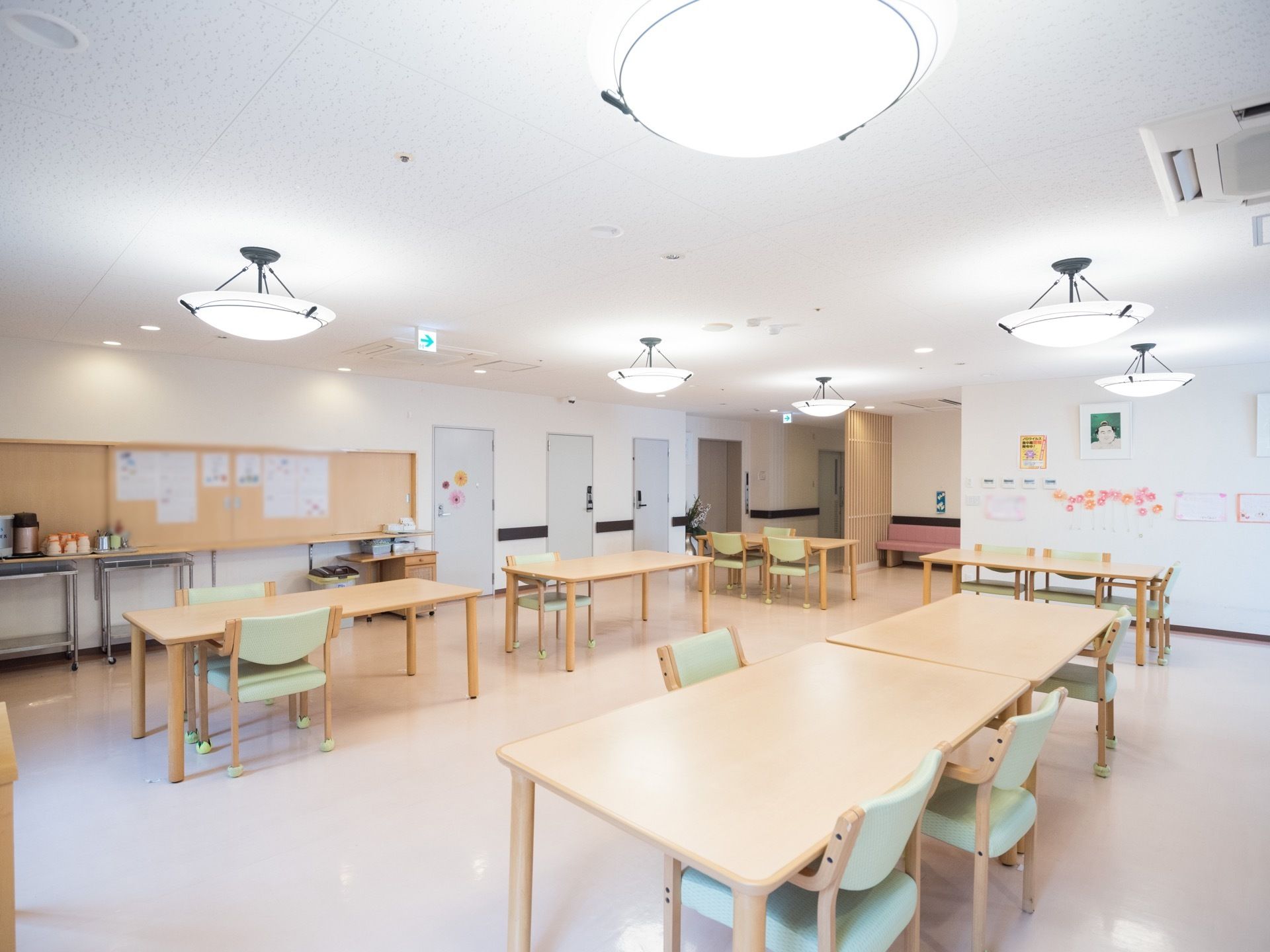 広々とした空間に、複数のテーブルや椅子が並べられている。掲示板が設置された壁の手前に、ポットや食器を載せたテーブルが置いてある。