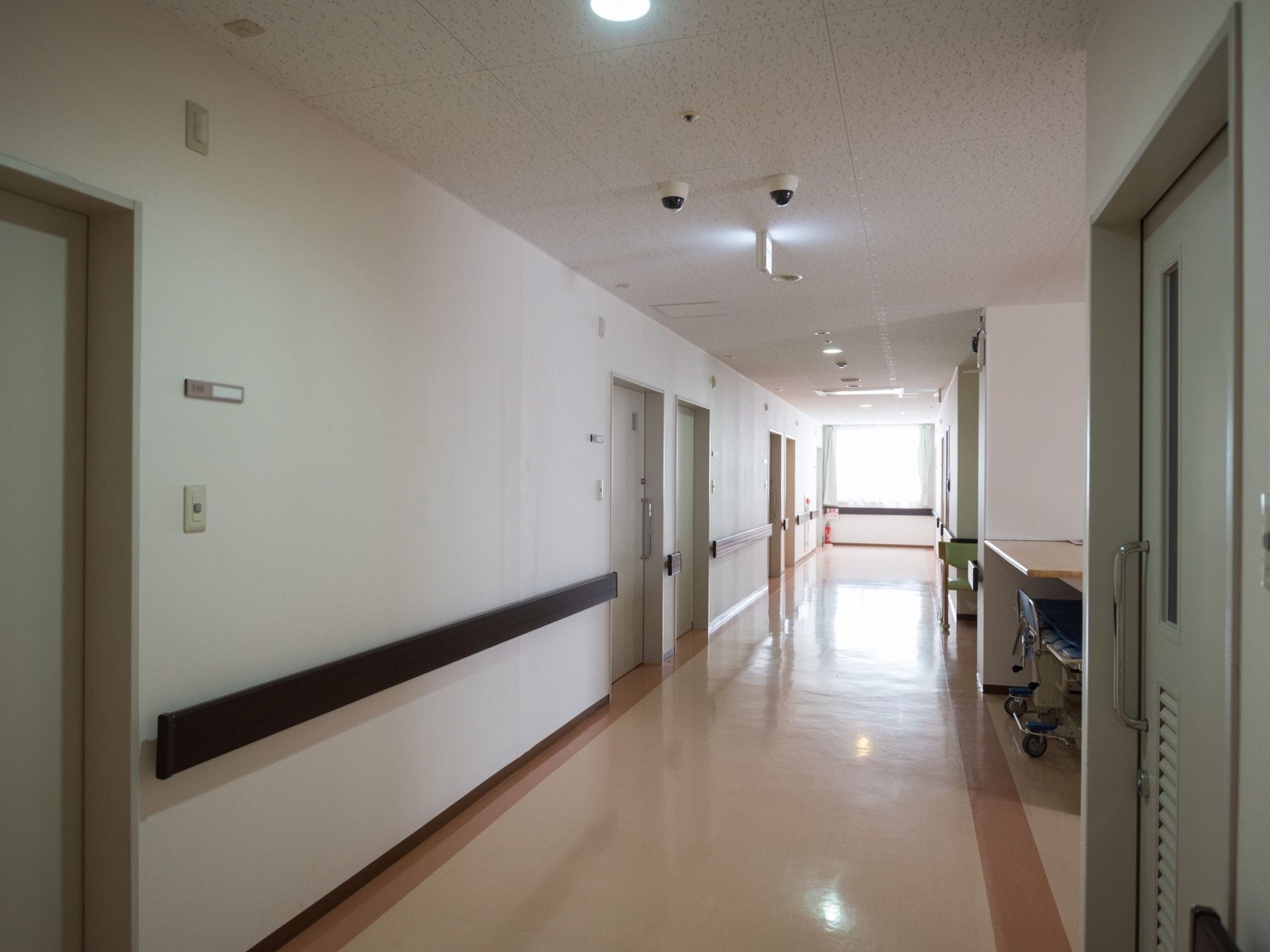 両側の壁面に淡い緑色の引き戸が並んでいる通路である。突き当たりに窓があり、外光が射し込んでいて明るい。