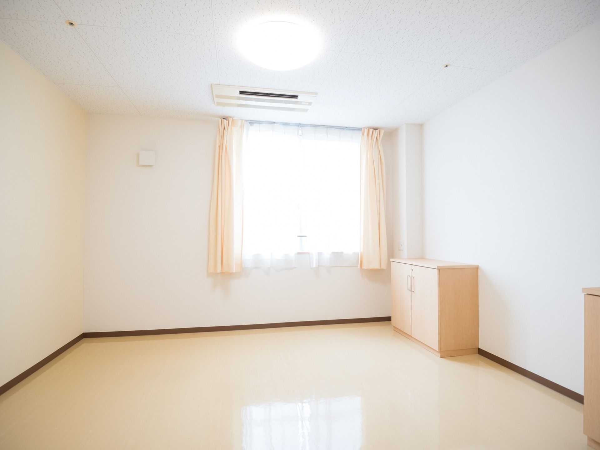 明るい色味の艶のある床が施された個室に、木製の収納家具が置いてある。エアコンが天井に埋め込まれている。