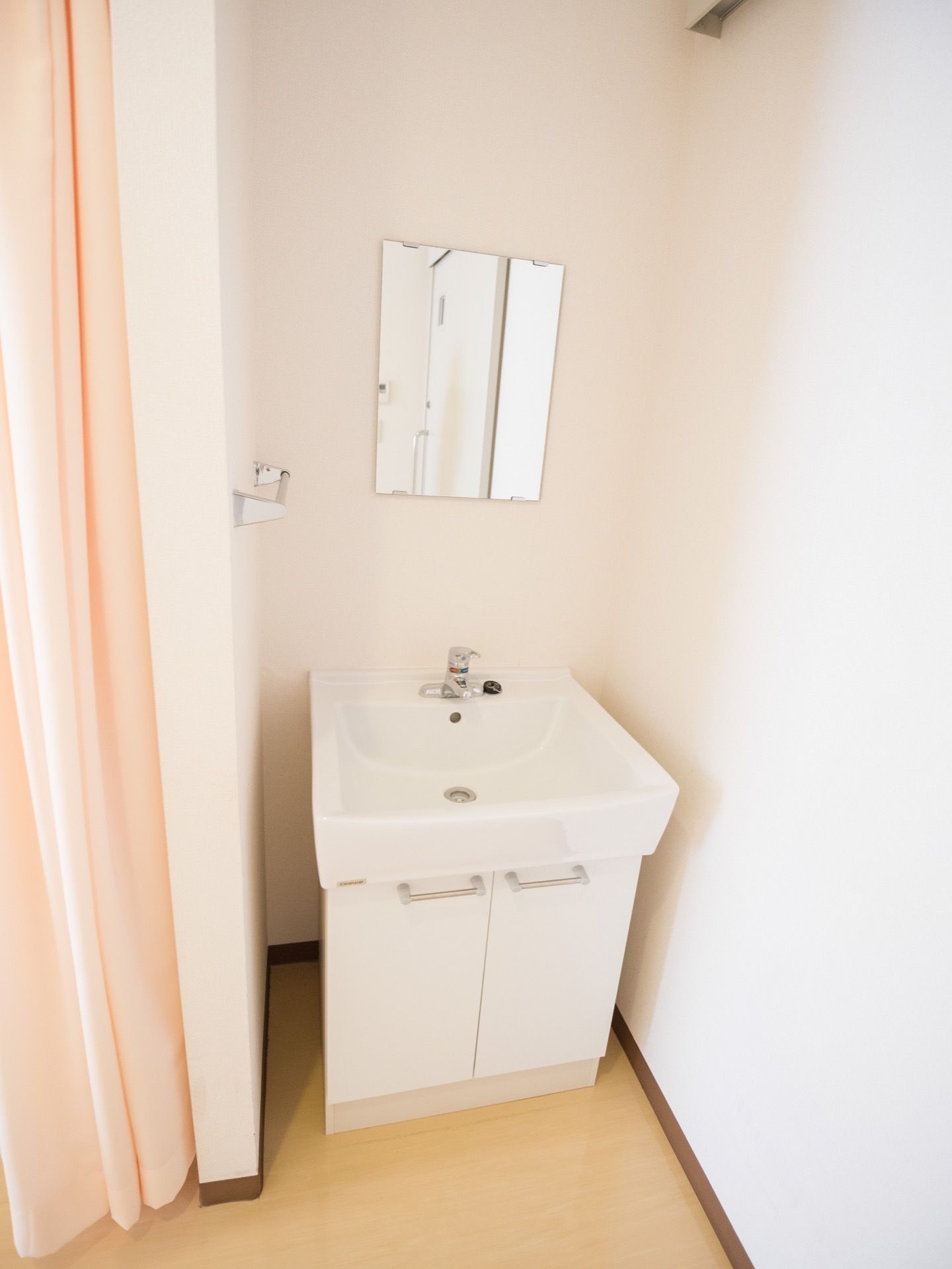 部屋の一角に、白く四角い洗面台が設置されている。正面の壁には鏡が取り付けてあり、左側にタオルハンガーがある。