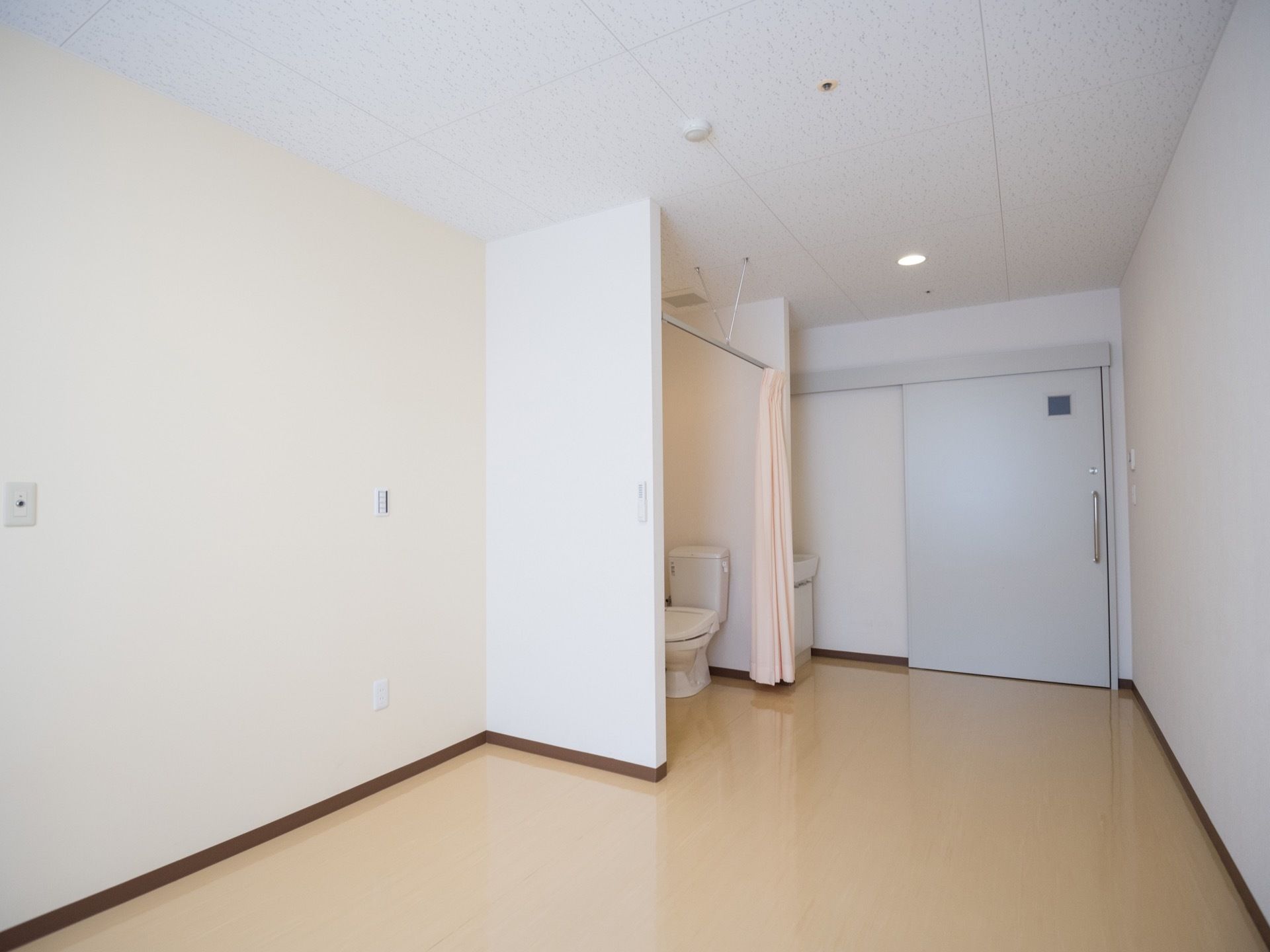 部屋の一角がピンク色のカーテンで仕切られており、洋式便器が据えてある。トイレスペースの奧に洗面台が見える。