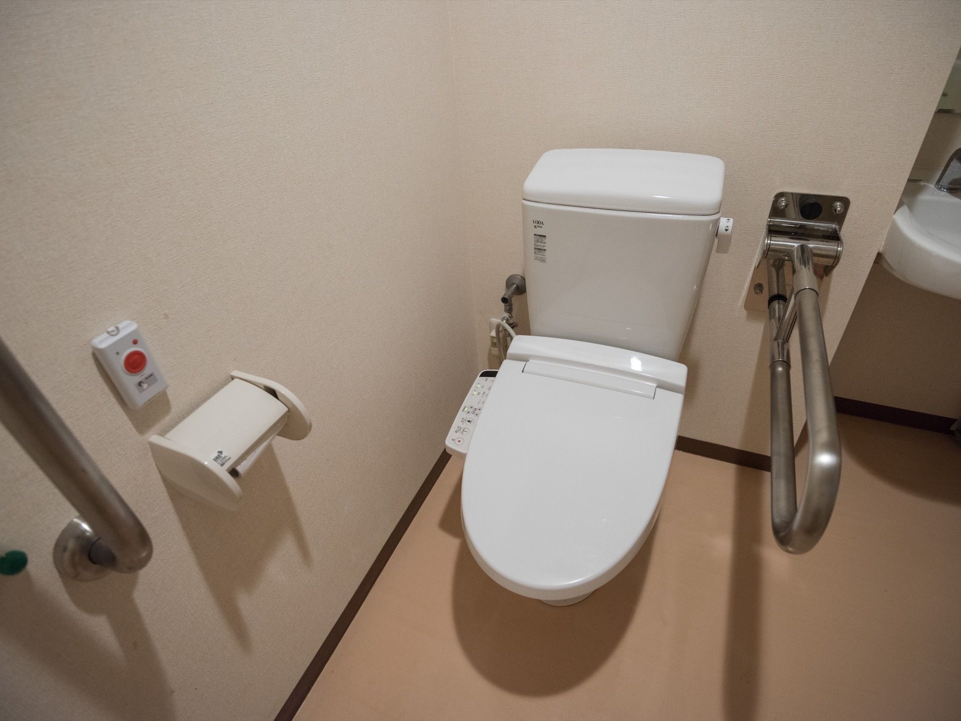 タンクや蓋が付いた洋式便器が据えてあり、その両側にステンレス製の手すりが設置されている。トイレットペーパーホルダーの上に押ボタンがある。