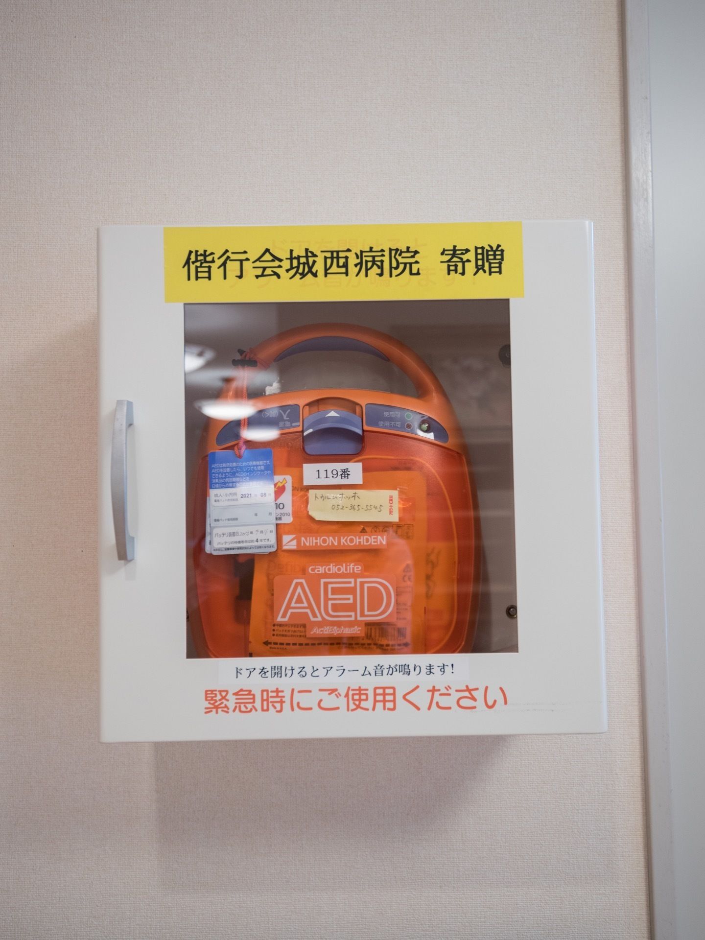 壁面に設置された自動体外式除細動器。機器を寄贈してくれた病院、緊急時の連絡先などがラベリングされている。