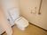 カーテンで仕切られたフローリングの一角に洋式便器が据えてある。壁面にはトイレットペーパーホルダーの他に、押ボタンや手すりが設置されている。