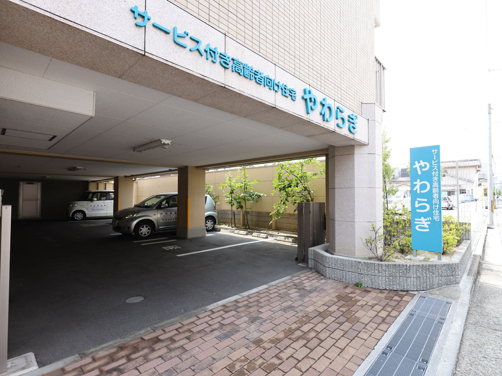 自然豊かな場所を車いすで散歩している高齢男性とそれを補助しながら話している女性スタッフ