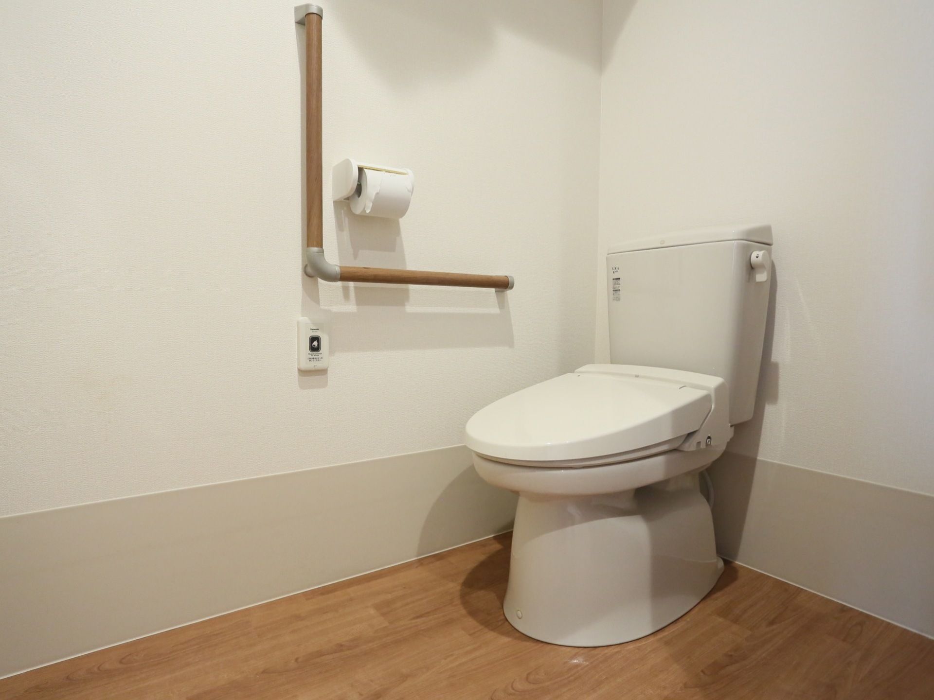 トイレはふたつきの便座になっている。トイレットペーパーホルダーを囲むように、縦横つながった手すりが設置されている。