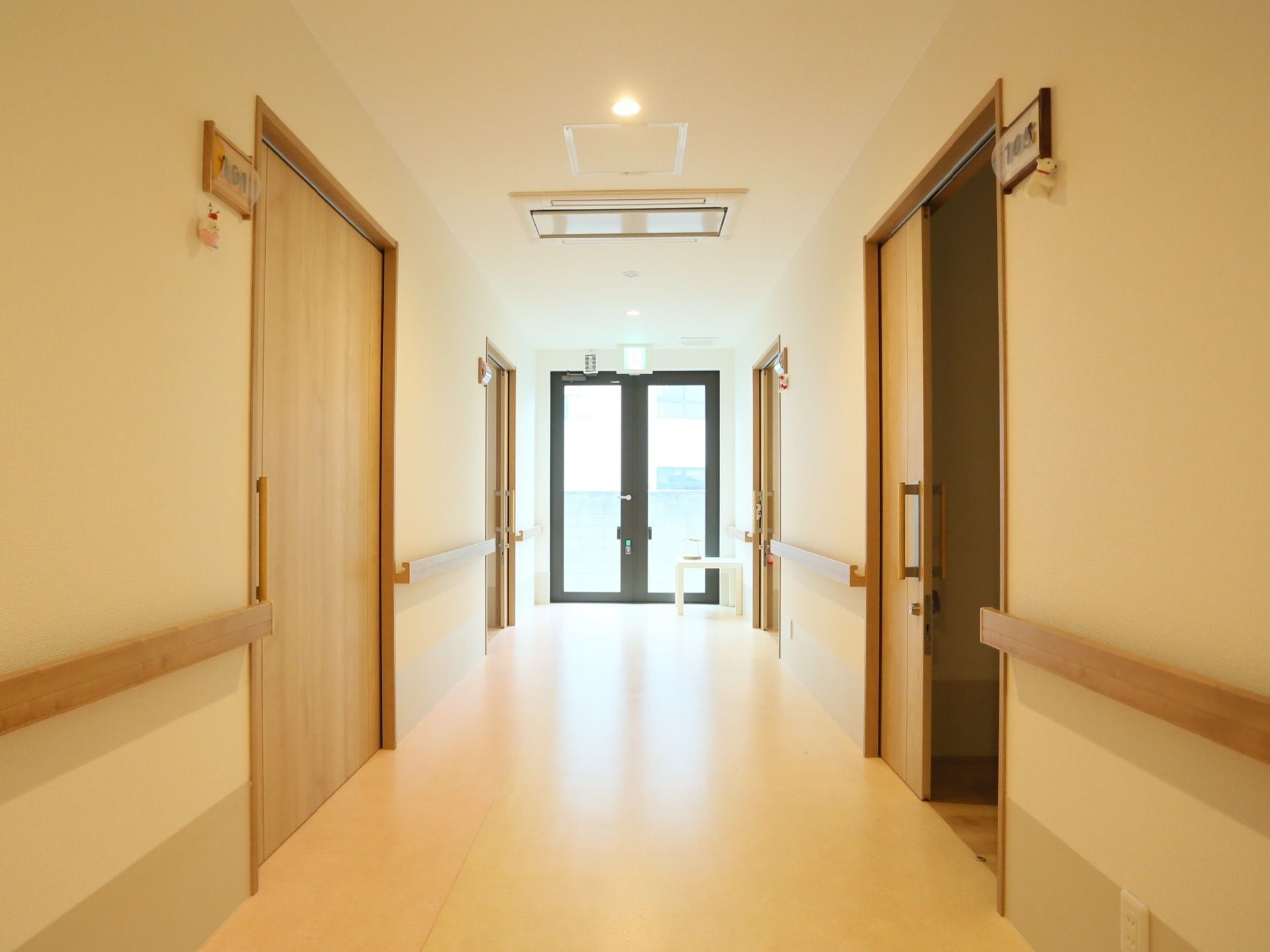 廊下の天井には、埋め込み式の暖色系の照明が設置されている。つきあたりの掃き出し窓は非常口になっている。