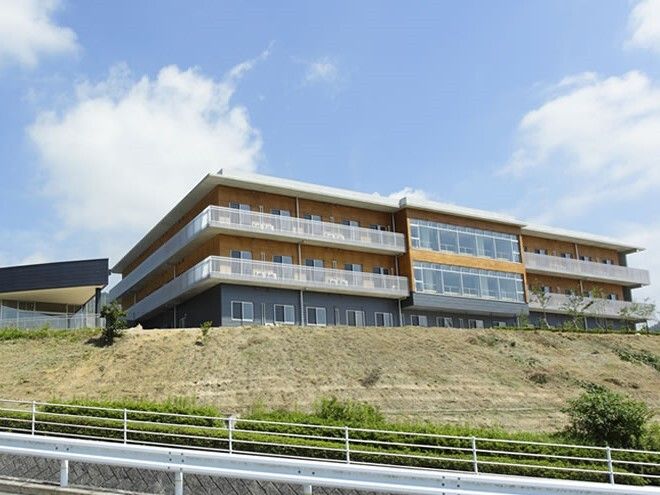 各フロアにベランダが付いた3階建ての建物はグレー系の外観。高台に建っている。