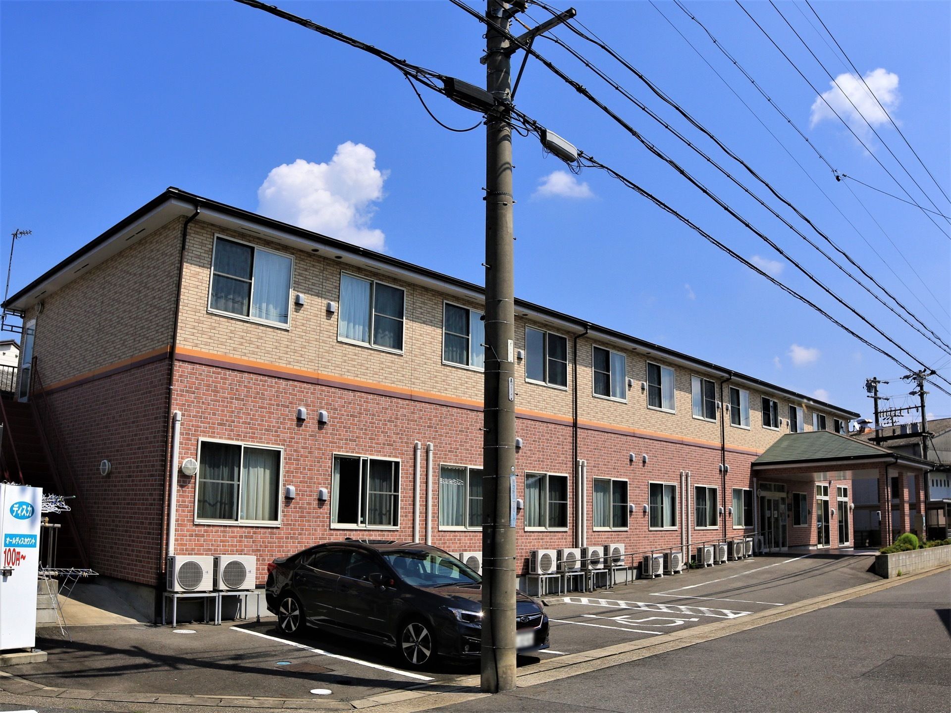 淡いピンクとベージュの２階建ての建造物である。駐車場が完備されており、玄関まで乗り付けることができる。
