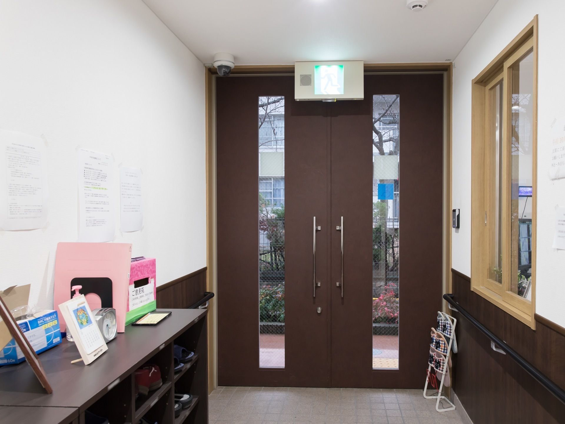 内側から見た玄関口。ドアの上には非常口のランプが取り付けてある。天井には監視カメラが設置されている。
