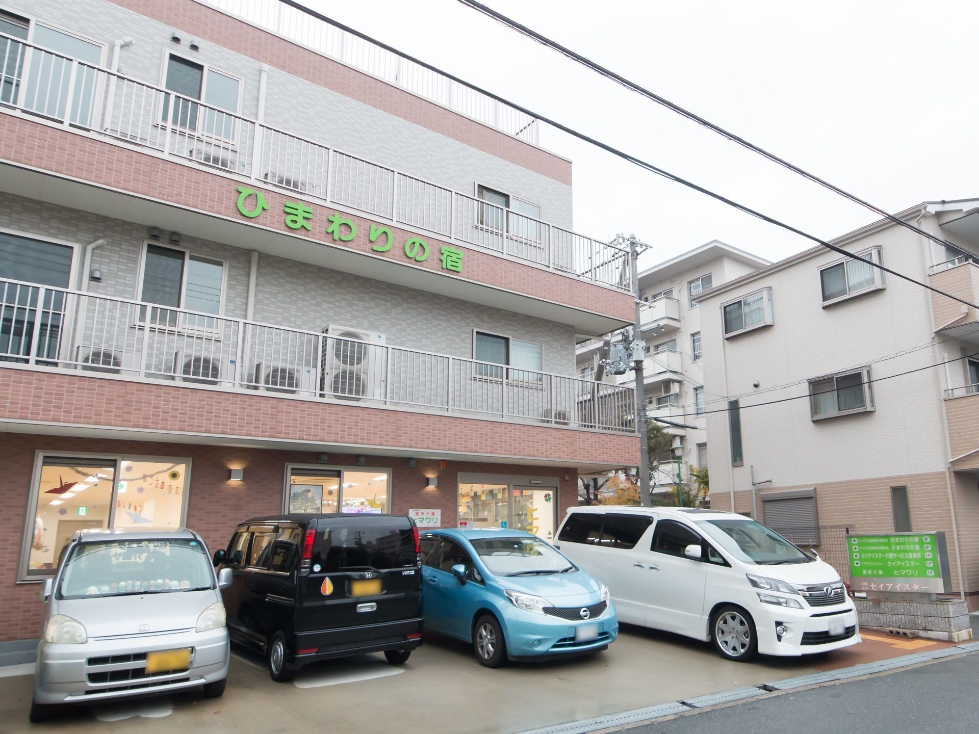 施設の入る建物は３階建て構造になっている。敷地内にあるライトグリーンの看板には、併設の設備も表示してある。