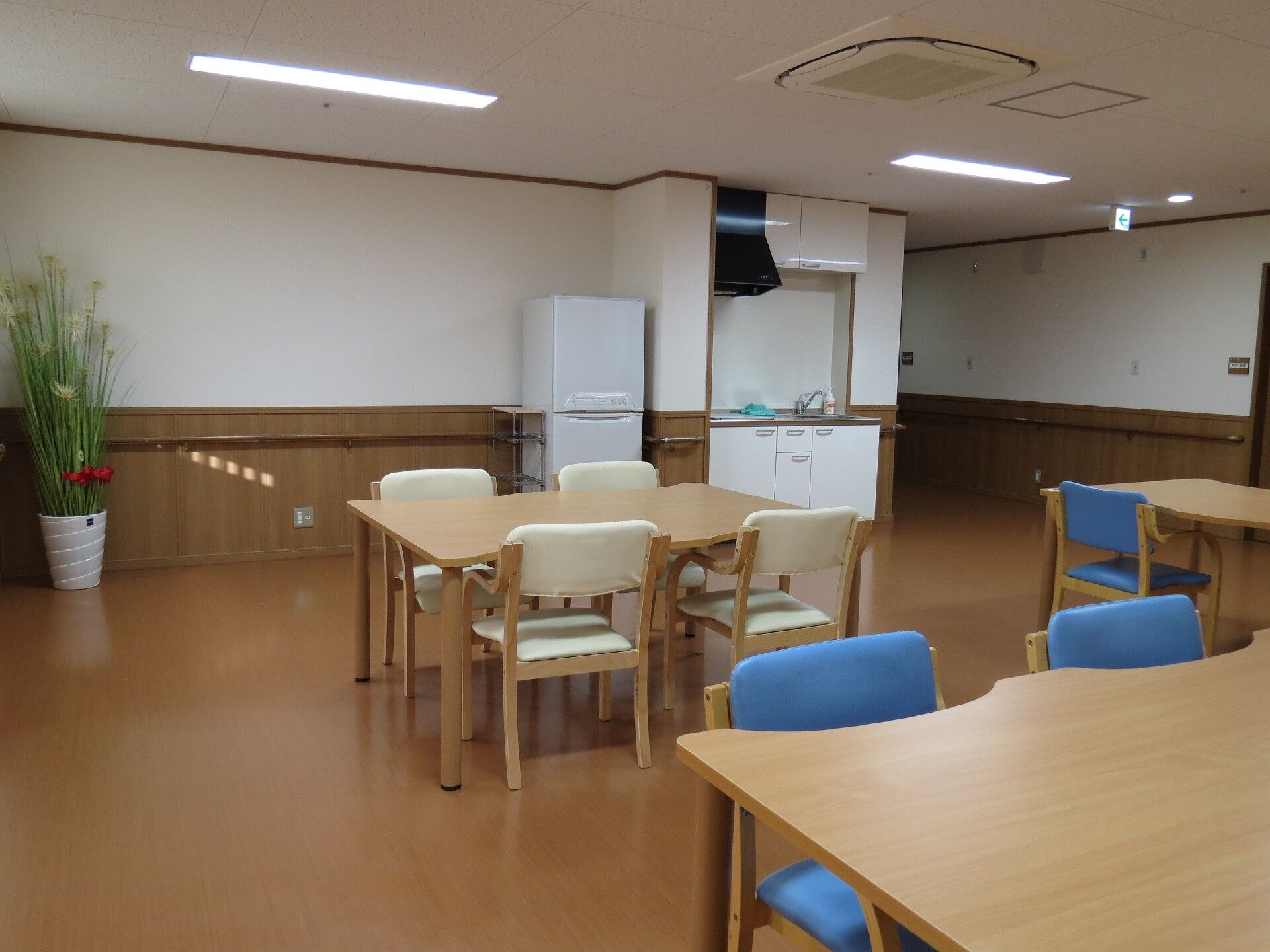 青や白の椅子がセットされた少人数用のダイニングテーブルが複数置かれた食堂には大きな冷蔵庫があり、キッチンも付いている。